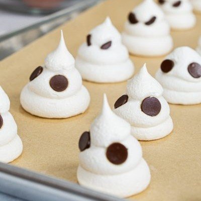 12 Best Halloween Desserts 9 A tray of ghost-shaped meringue cookies decorated with black eyes, surrounded by colorful candy.