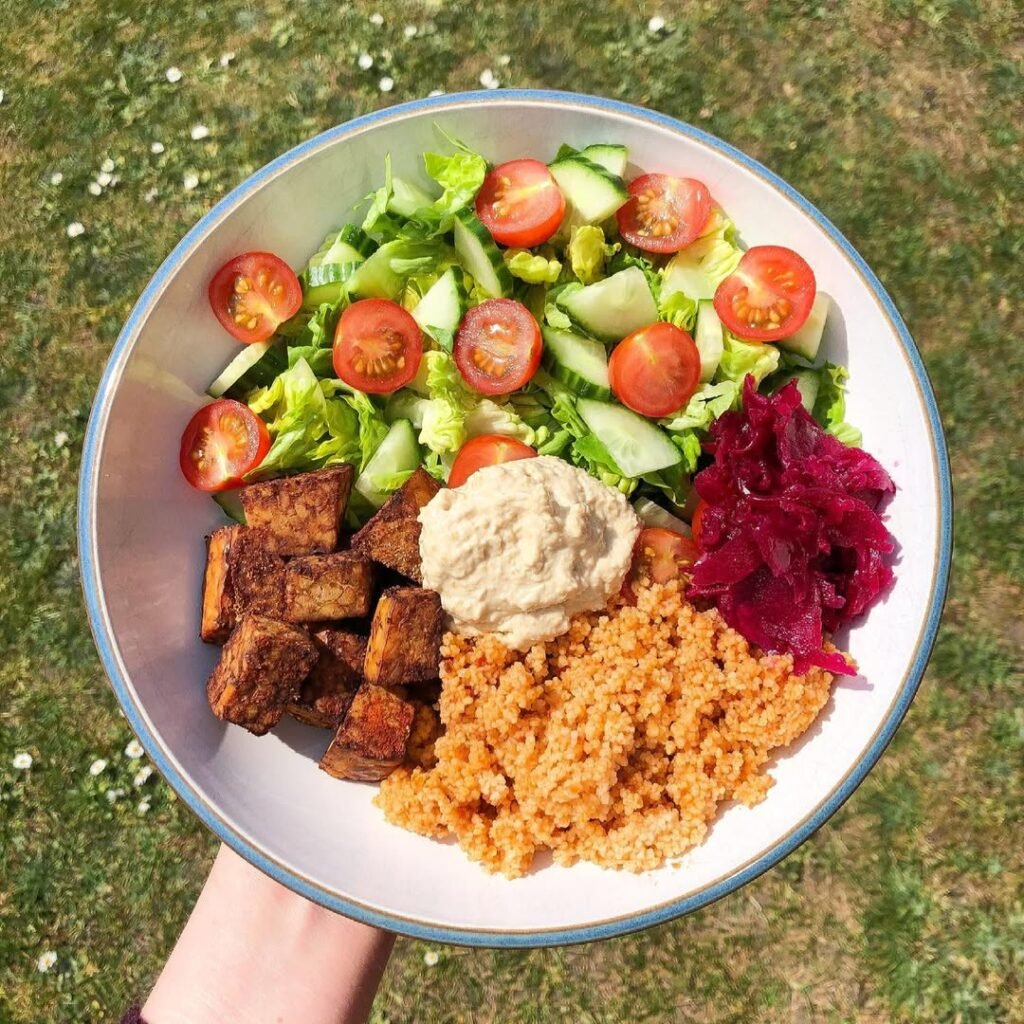 A colorful Vegan Buddha Bowl filled with grains, roasted sweet potatoes, black beans, and greens, topped with tahini sauce.