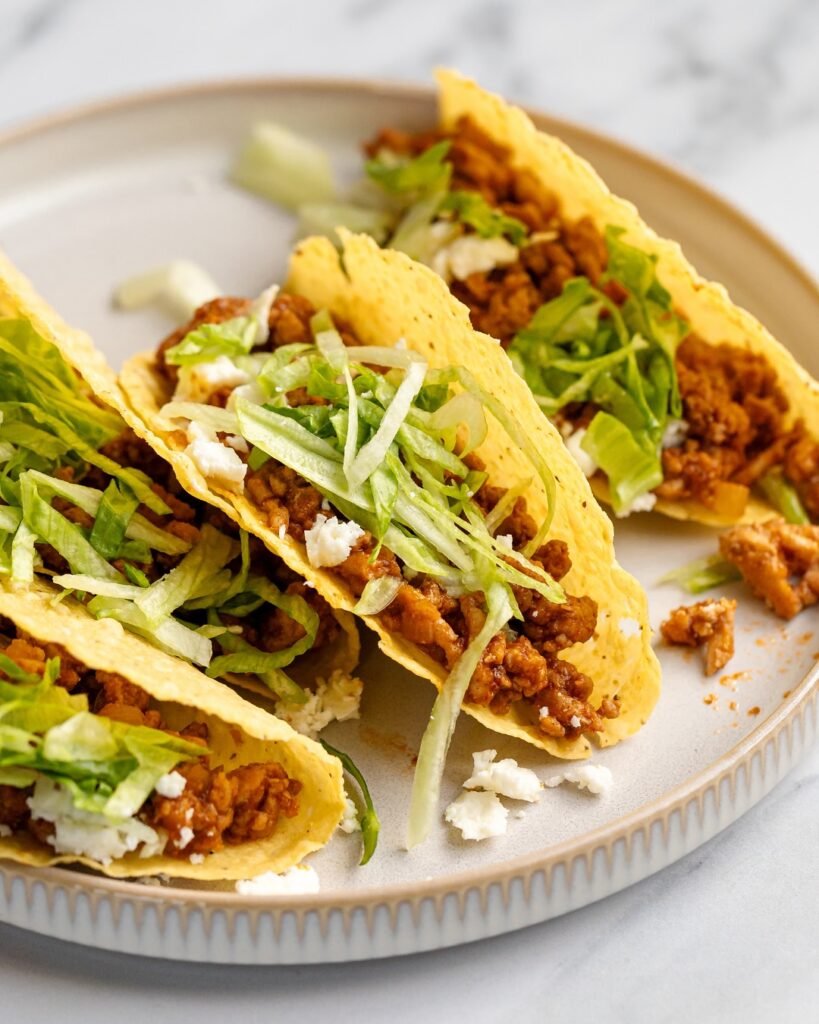 Spicy ground chicken tacos with avocado crema, garnished with cilantro and lime wedges.