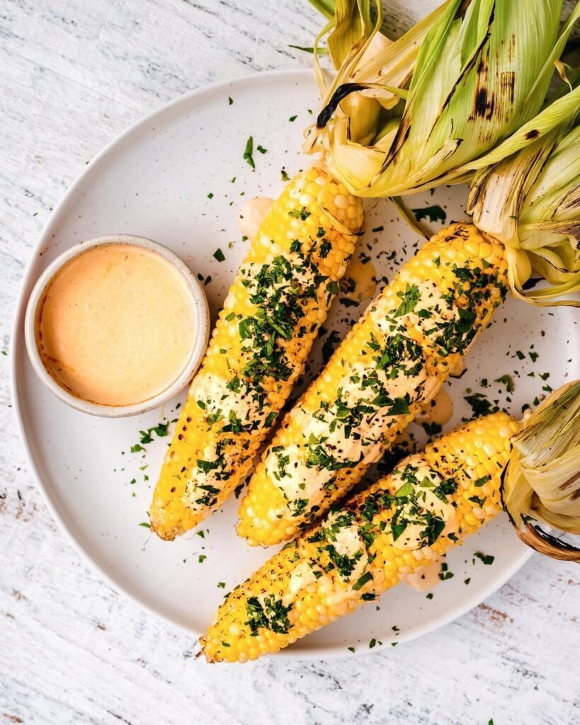 5 Fall Grilling Recipes To Warm Up The Chilly Season 5 Grilled corn on the cob with herbs, set against a sunset background