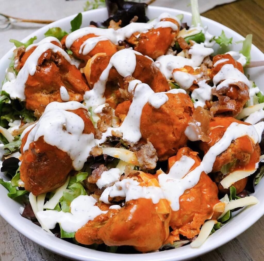 A platter of Cauliflower Buffalo Wings with celery sticks and a creamy dip.