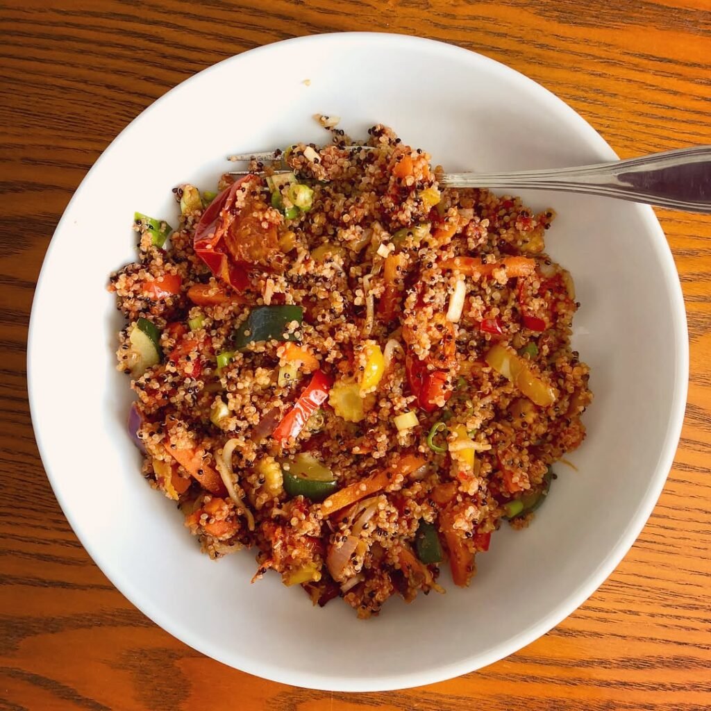A bowl of roasted vegetable quinoa with tahini sauce and fresh herbs.