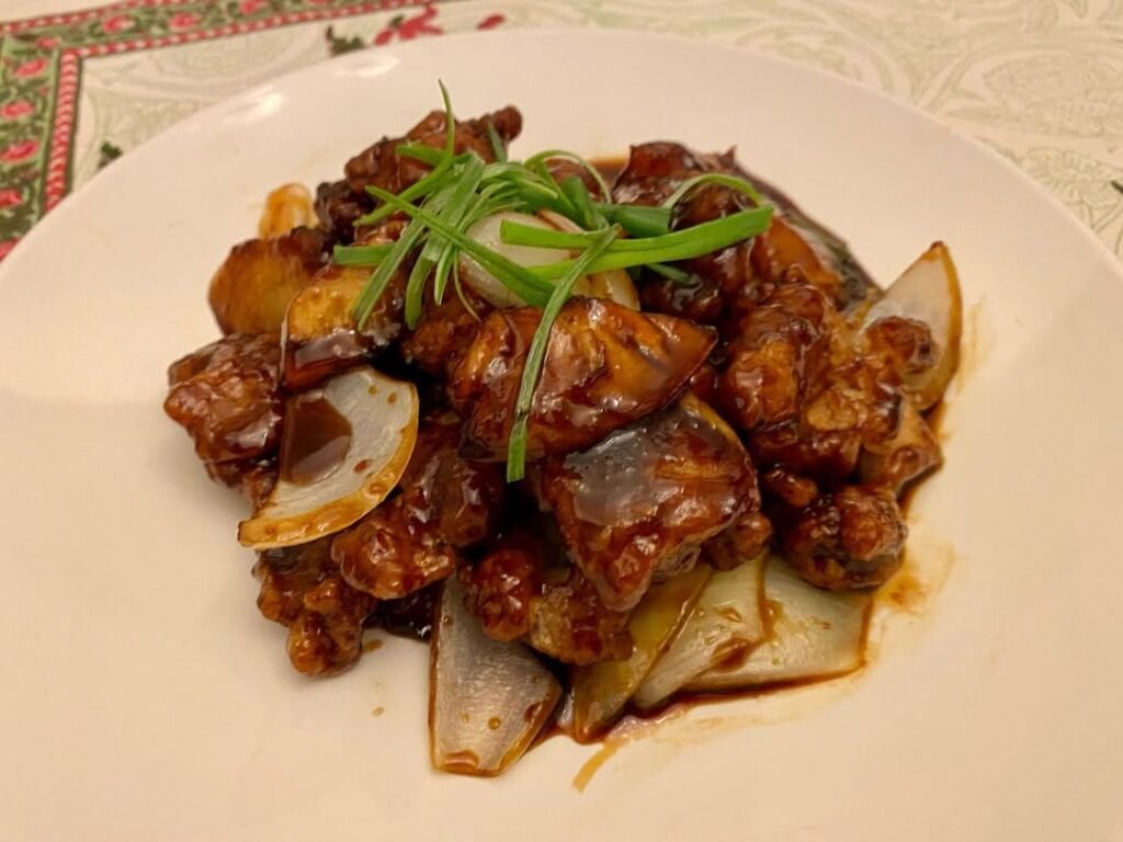 4 Chinese Sweet And Sour Chicken Recipes 2 A plate of crispy sweet and sour chicken with pineapple, served over rice, garnished with green onions and colorful bell peppers.