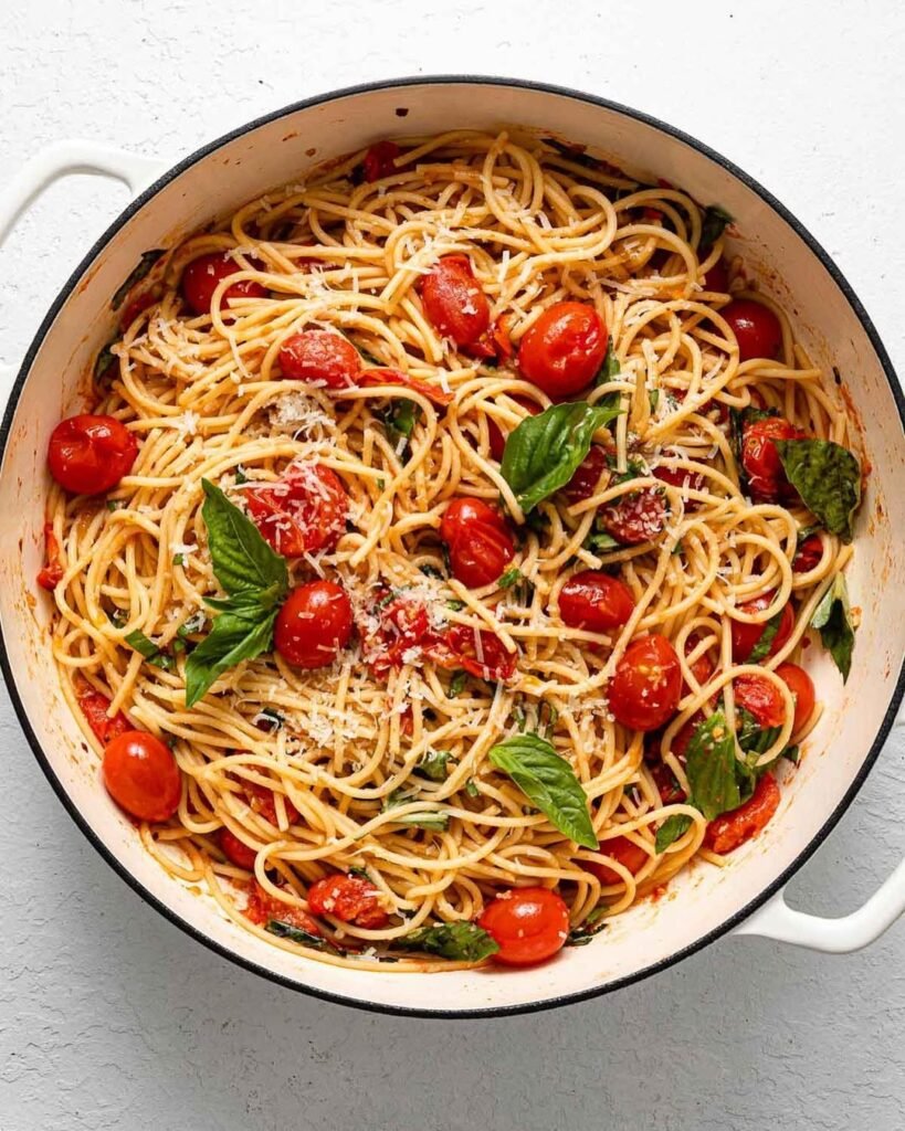 A bowl of creamy tomato basil pasta topped with fresh basil and cherry tomatoes.