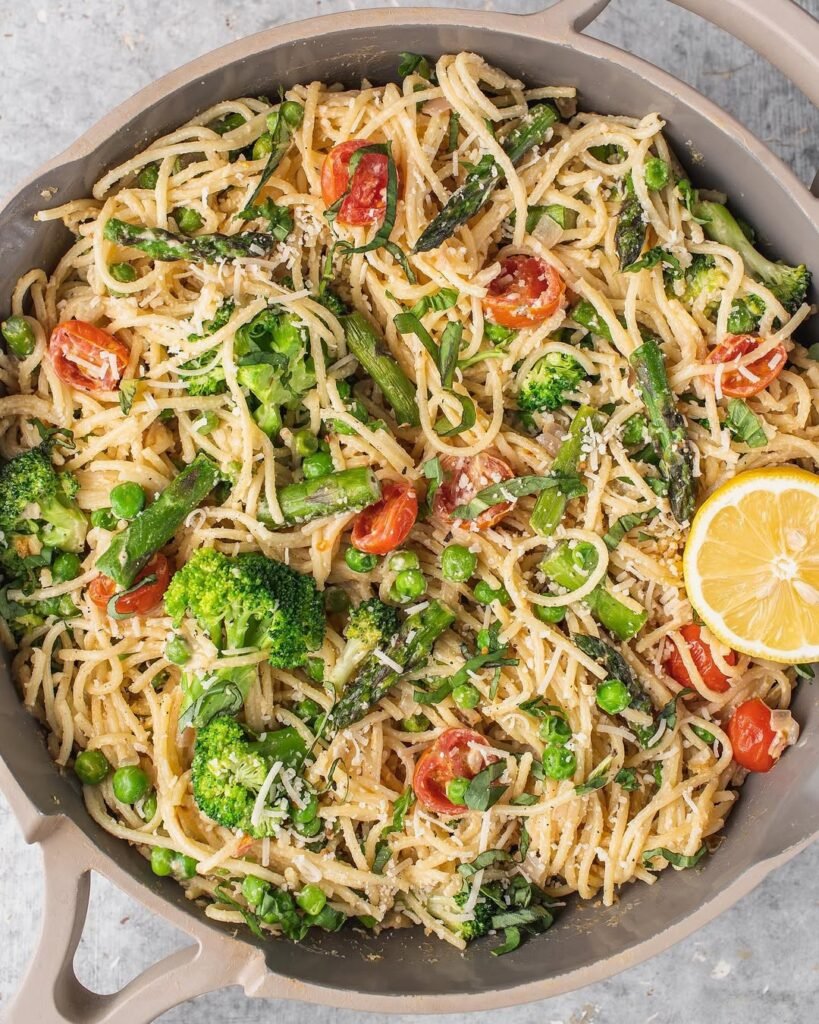 A bowl of creamy vegan pasta primavera with colorful vegetables and fresh herbs