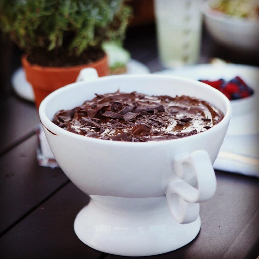 A glass of chocolate avocado mousse topped with fresh berries and mint leaves