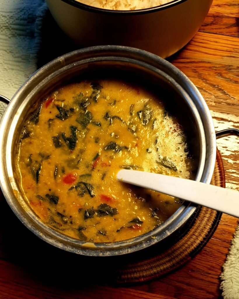 A bowl of lentil soup with spinach and diced vegetables, served with a slice of bread.