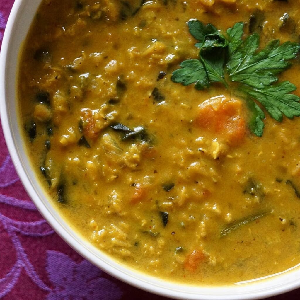 A bowl of lentil soup with spinach, accompanied by slices of bread.