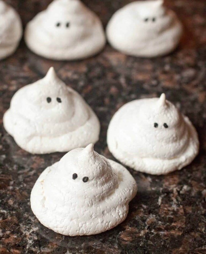 9 Best Halloween Party Treats Sure To Spook Your Guests 3 Plate of ghost-shaped meringue cookies with chocolate chip eyes, surrounded by autumn leaves and a pumpkin.