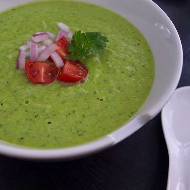 A bowl of chilled avocado and cucumber soup garnished with herbs and cucumber slices.
