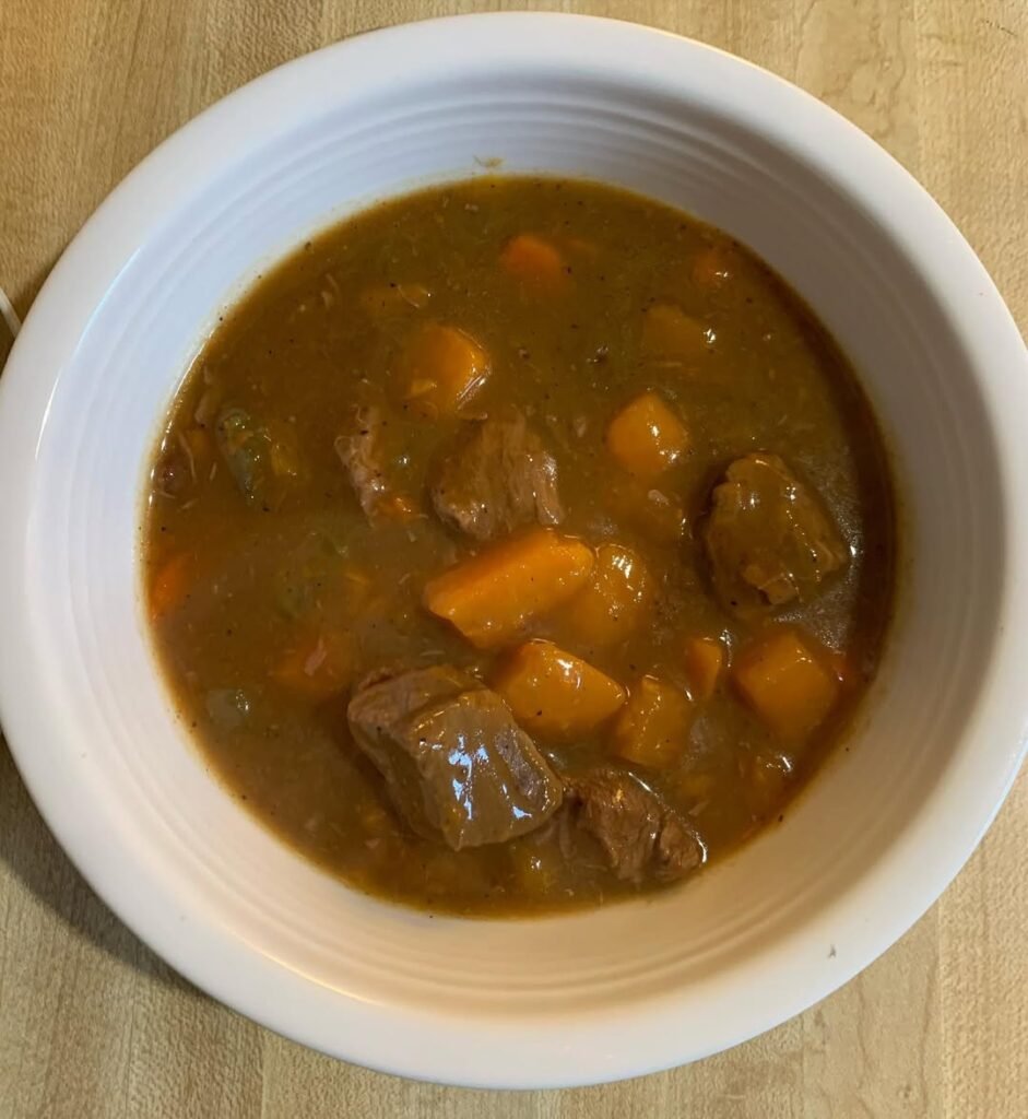 A pot of beef and sweet potato stew cooking on the stovetop.
