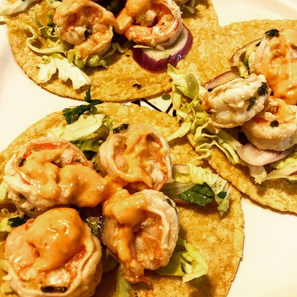 Cilantro lime shrimp tacos with cabbage and lime wedges on a wooden board