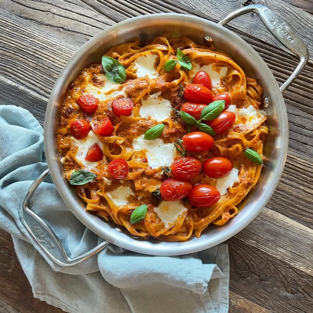 A bowl of creamy tomato basil pasta with cherry tomatoes and fresh basil on a wooden table.