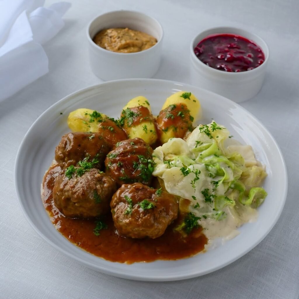 A plate of Scandinavian Kjøttkaker with cream sauce, mashed potatoes, and lingonberry sauce.