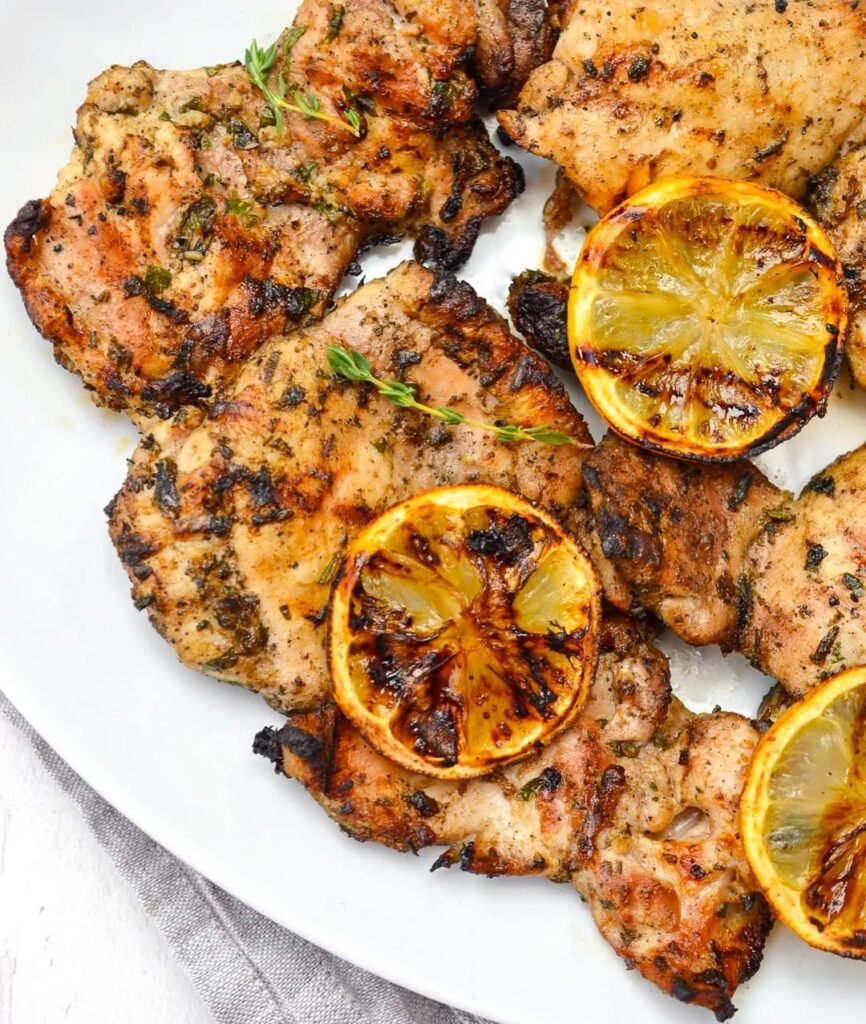 Grilled chicken breasts garnished with lemon slices and herbs