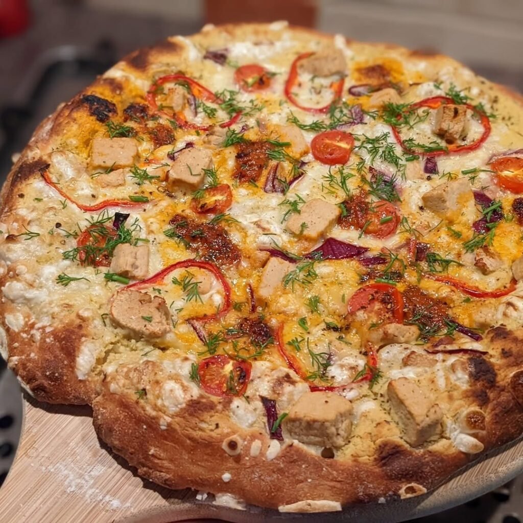 A delicious focaccia pizza topped with roasted vegetables and hummus, served on a colorful tablecloth.