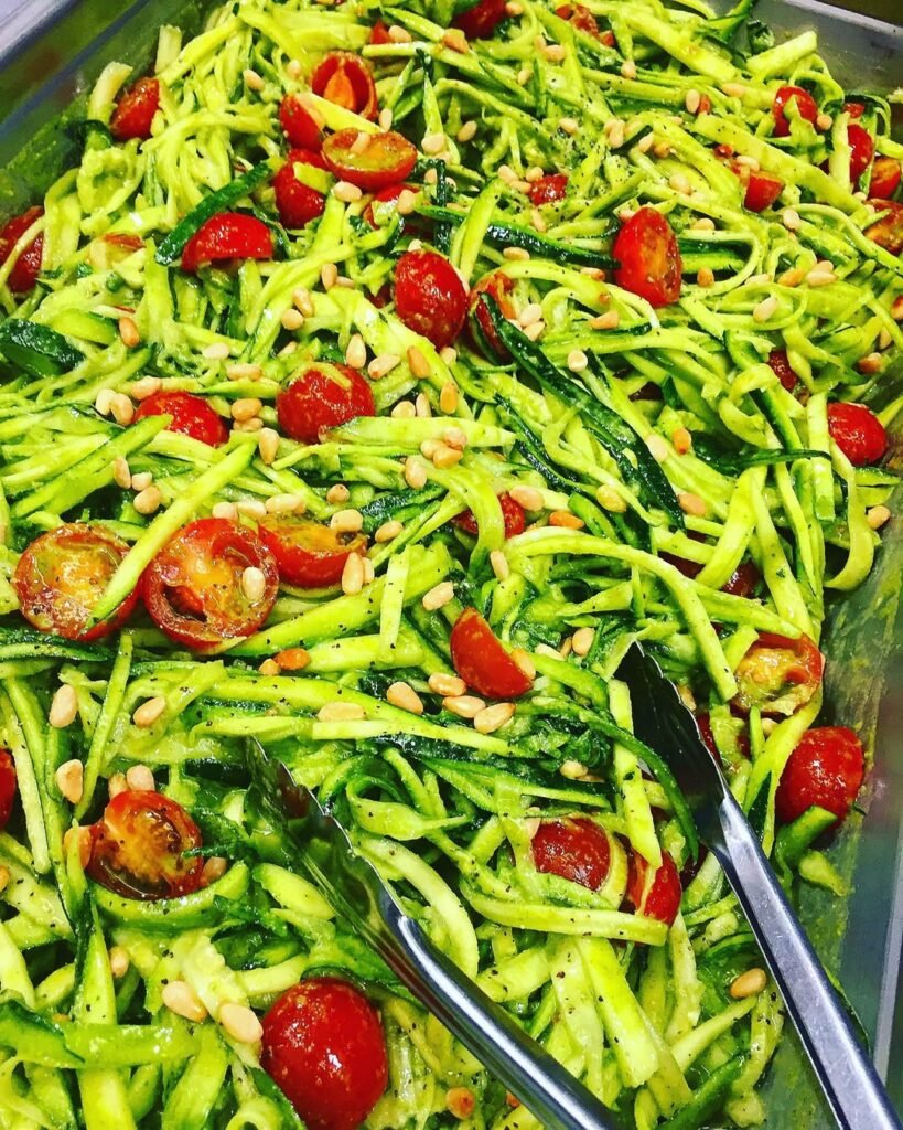 A bowl of zucchini noodles topped with avocado pesto and cherry tomatoes.