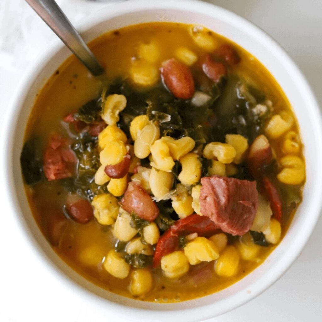A bowl of Cape Verdean Cachupa with pork and beans, surrounded by fresh vegetables.