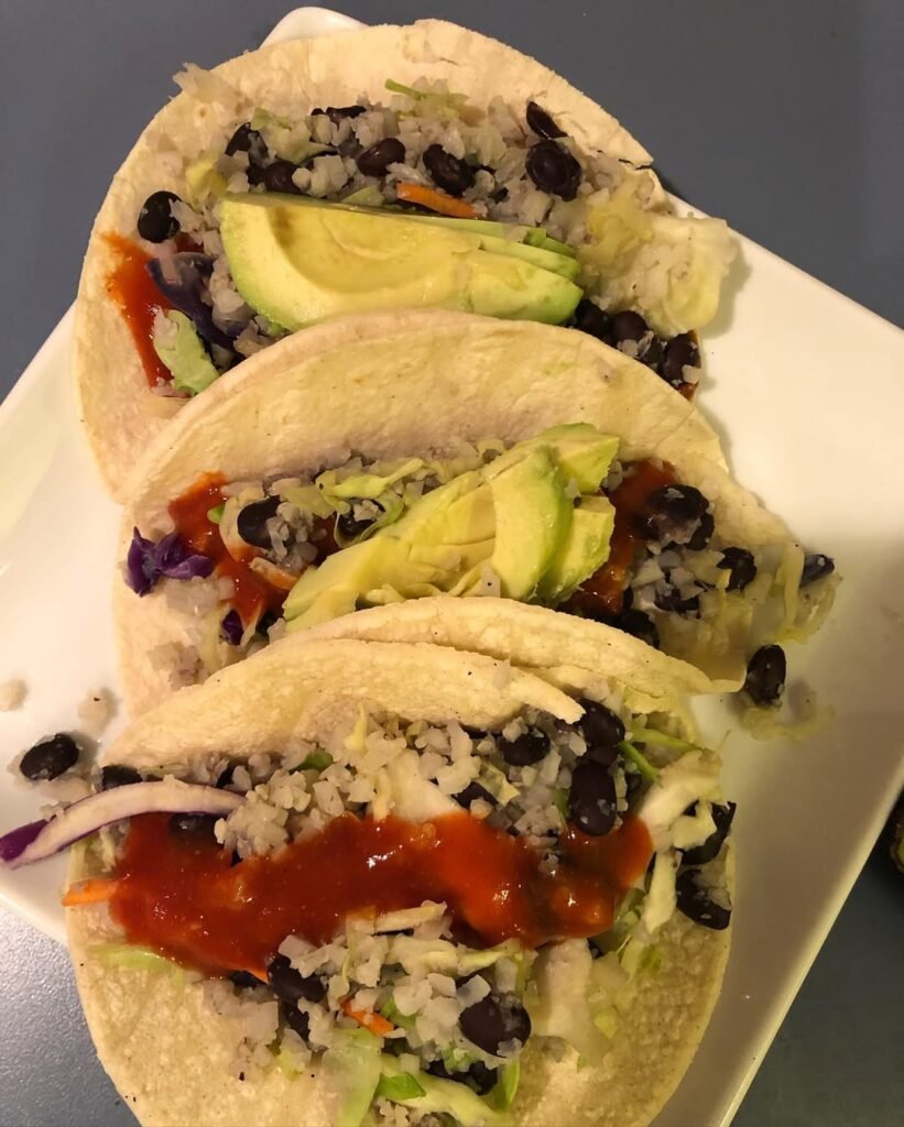 Cauliflower rice tacos filled with black beans, tomatoes, and avocado on a wooden board.