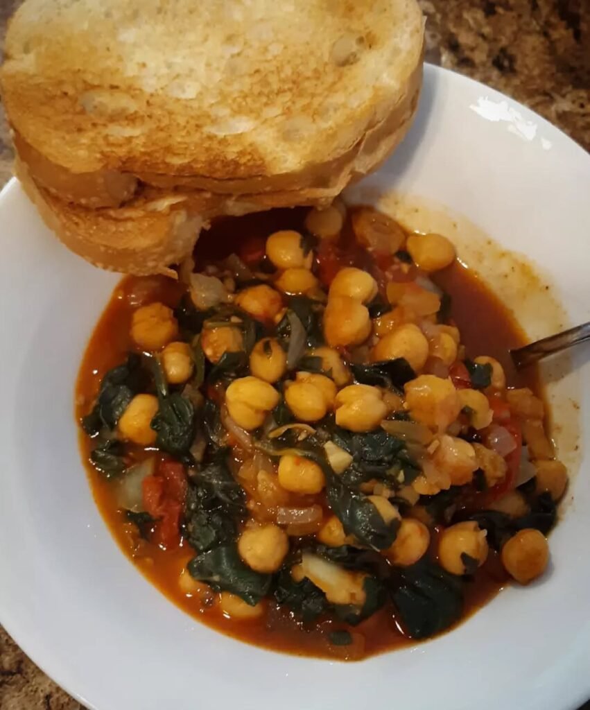 A bowl of chickpea and spinach stew with bread on the side.