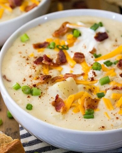 12 Creamy Potato Soup Recipes to Warm Your Soul 3 A bowl of creamy potato soup topped with bacon and chives, with a slice of bread on the side.