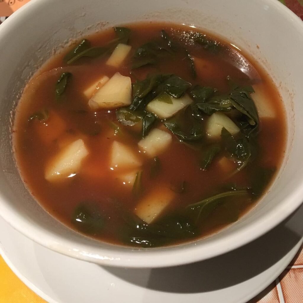 12 Creamy Potato Soup Recipes to Warm Your Soul 13 A bowl of creamy herbed potato soup with spinach, garnished with herbs and served with bread.