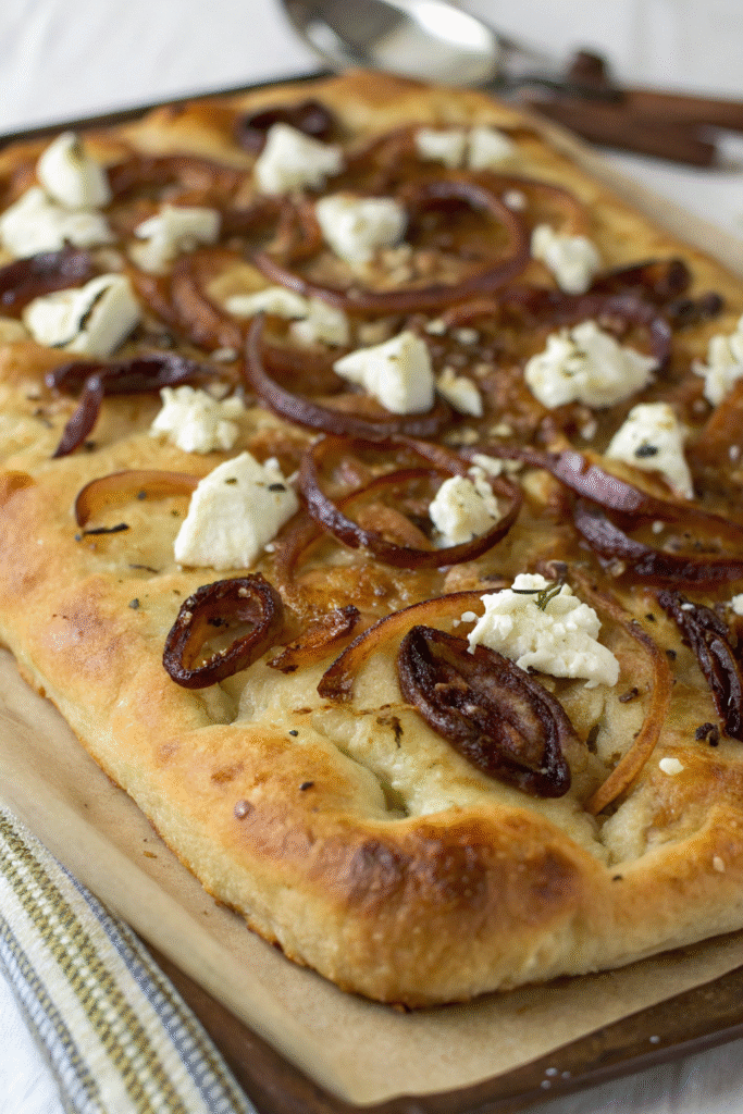 A slice of caramelized onion and goat cheese focaccia pizza on a plate, garnished with fresh herbs.