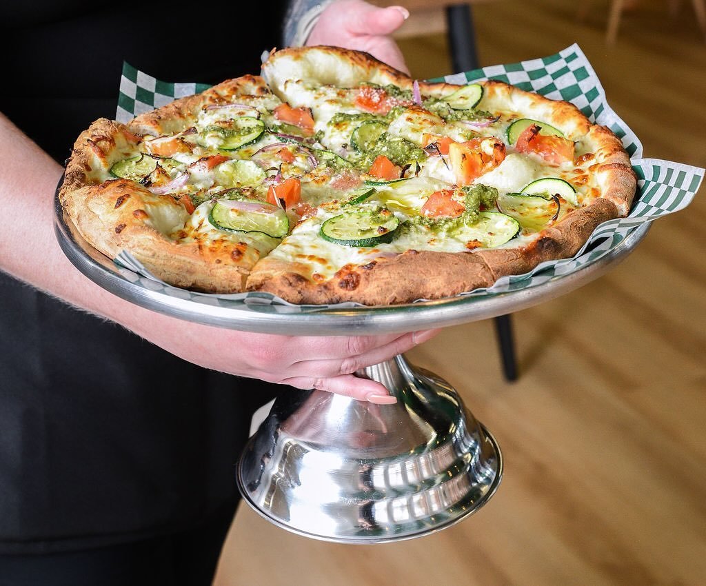A delicious roasted vegetable medley pizza on a wooden pizza peel.