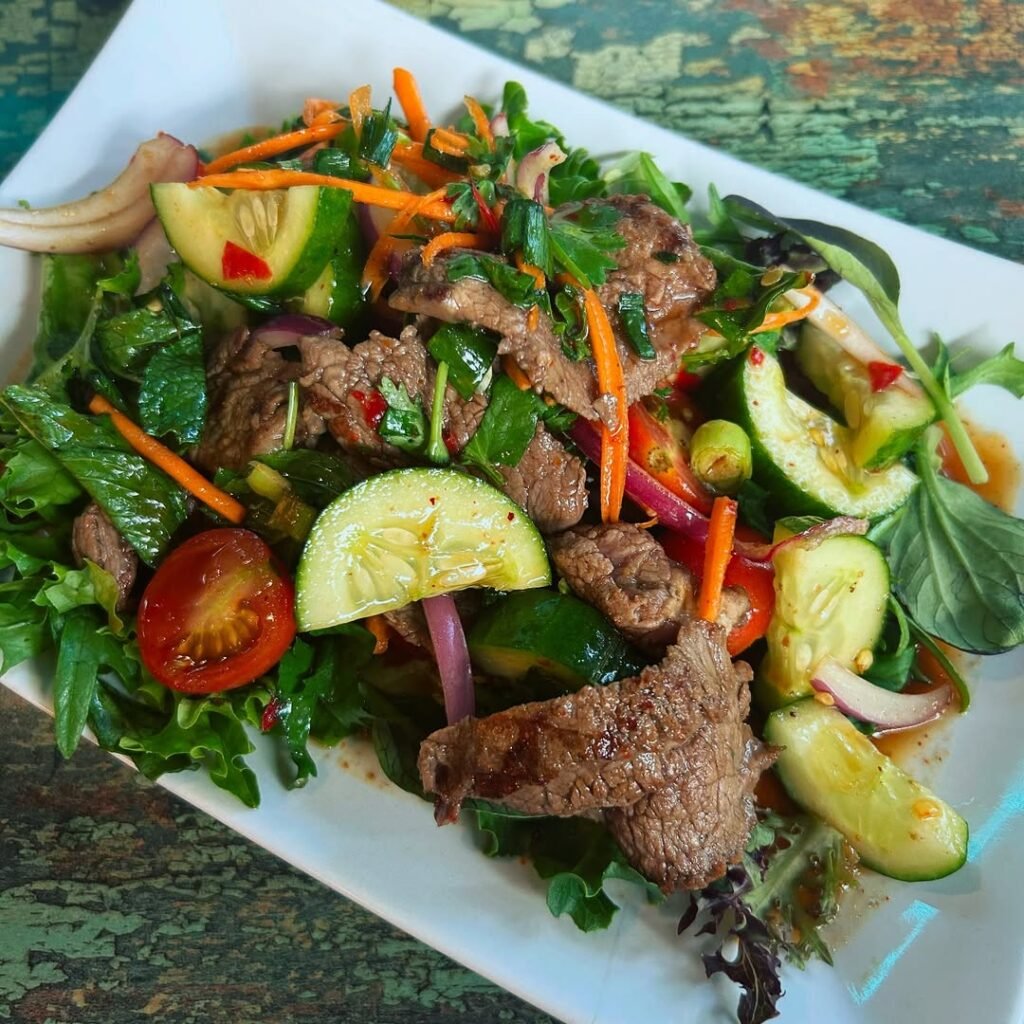 A colorful Thai beef salad with lime dressing in a glass bowl.