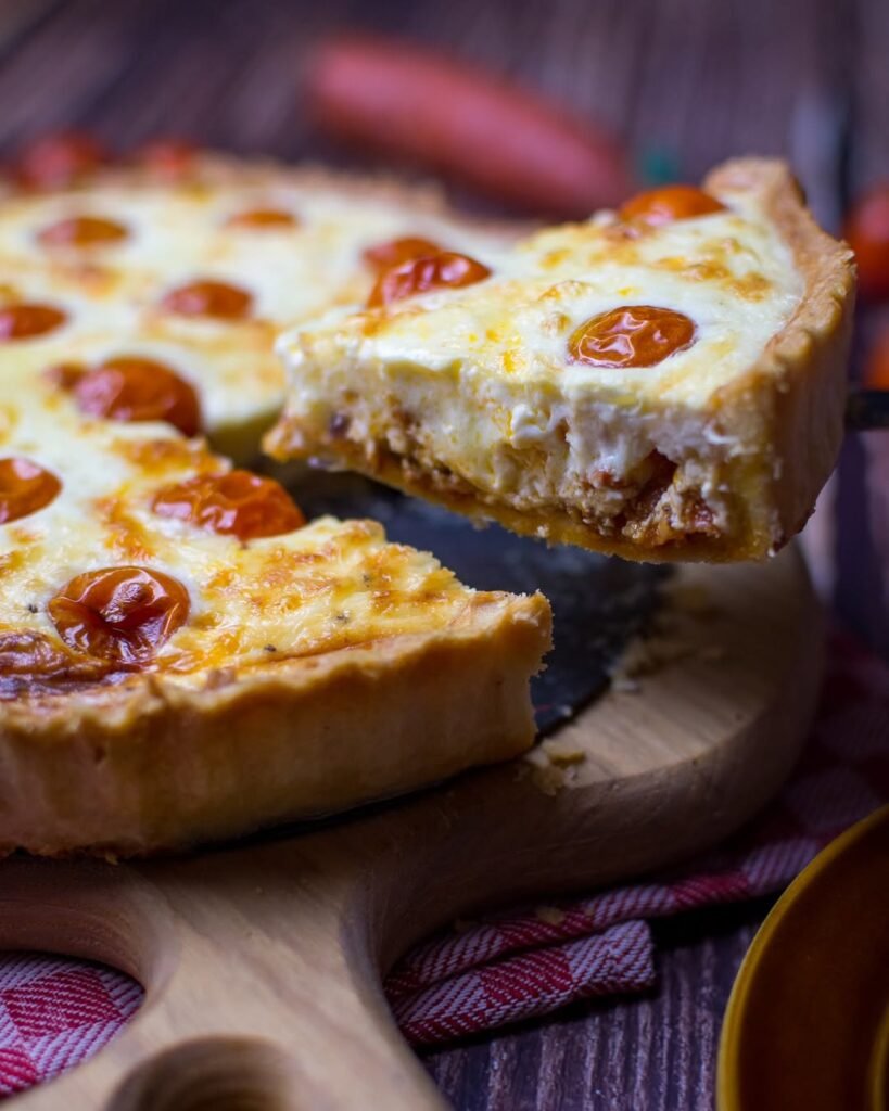 13 Delicious Recipes to Make with Tomato Soup 5 Slice of savory tomato soup quiche on a wooden plate, garnished with herbs.