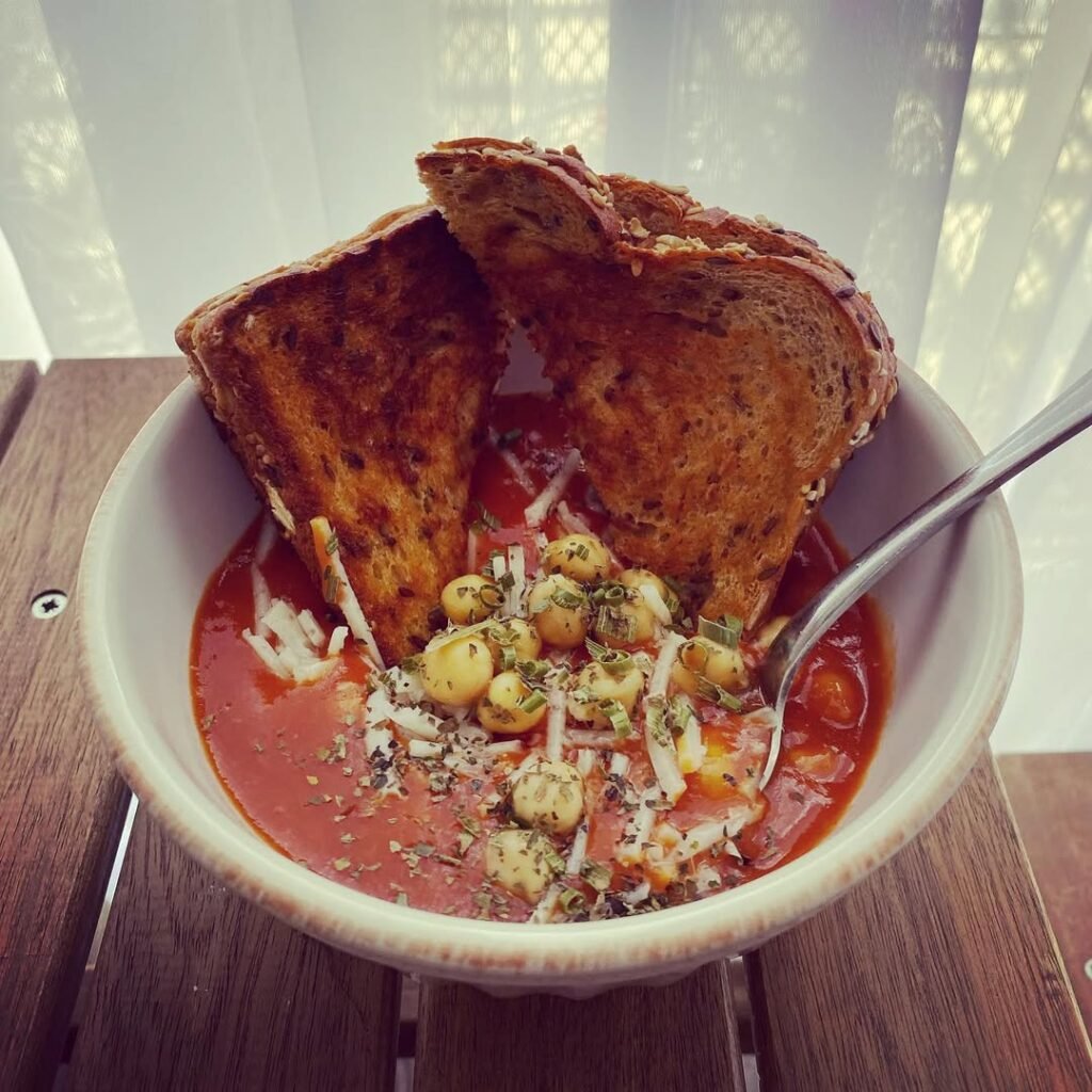 13 Delicious Recipes to Make with Tomato Soup 6 A bowl of spicy tomato soup with chickpeas, garnished with cilantro, next to a slice of bread.