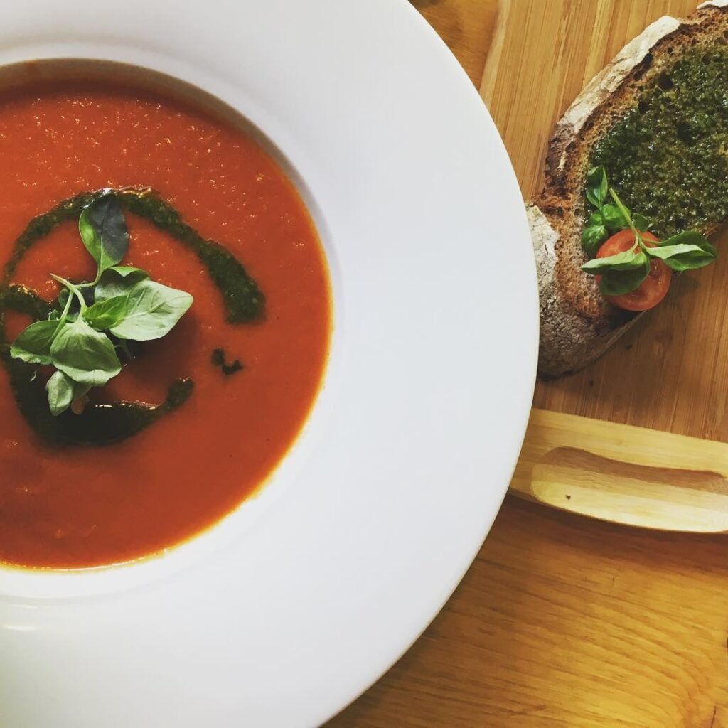 13 Delicious Recipes to Make with Tomato Soup 13 A bowl of tomato soup with a swirl of pesto and fresh basil leaves on the side.